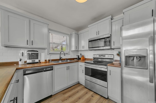 kitchen with appliances with stainless steel finishes, butcher block counters, white cabinetry, and a sink