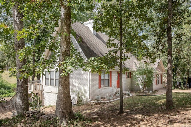 view of side of property featuring roof with shingles, brick siding, and a chimney