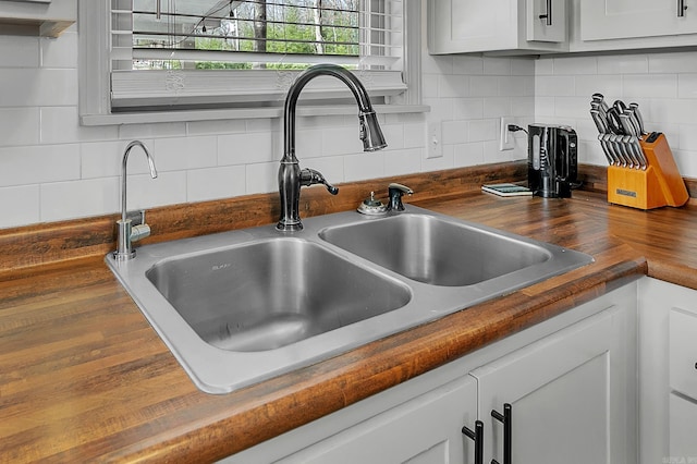 details featuring butcher block countertops, a sink, white cabinetry, and tasteful backsplash