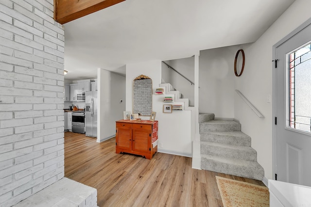 entryway with brick wall, light wood finished floors, and stairway