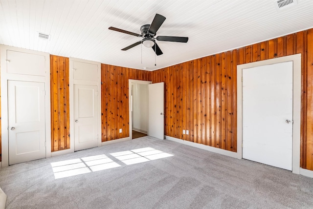 unfurnished bedroom featuring wooden walls, visible vents, and light colored carpet