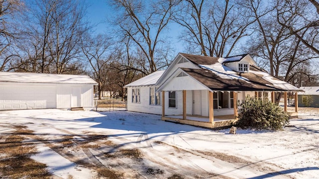 view of snowy exterior featuring an outbuilding, a porch, and a garage