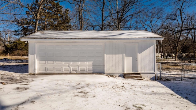 snow covered garage featuring a detached garage and fence