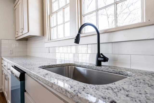 room details featuring light stone counters, backsplash, a sink, and stainless steel dishwasher