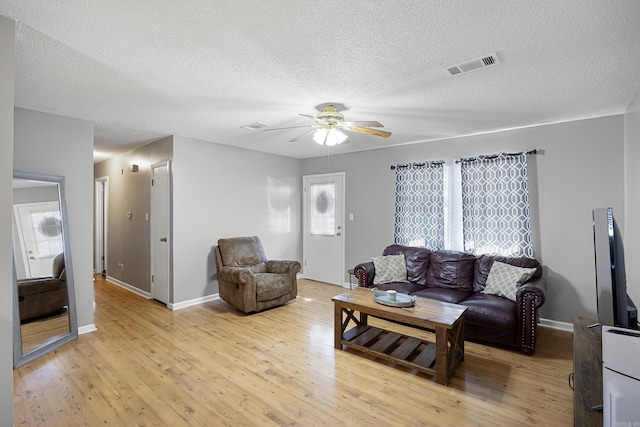 living room featuring a ceiling fan, visible vents, a textured ceiling, and light wood finished floors