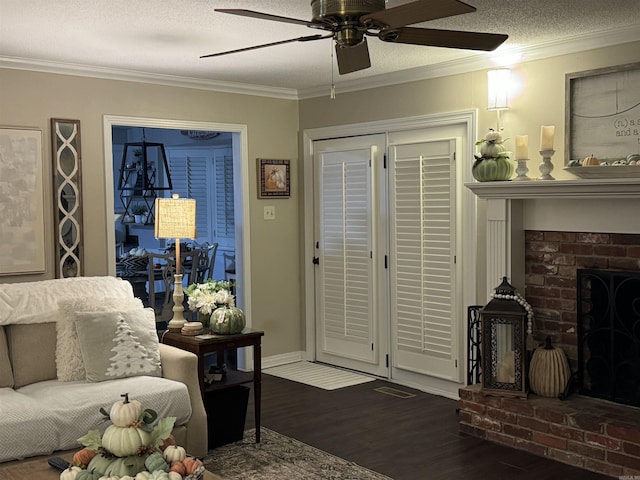 living area featuring a textured ceiling, dark wood-style flooring, a ceiling fan, a brick fireplace, and crown molding