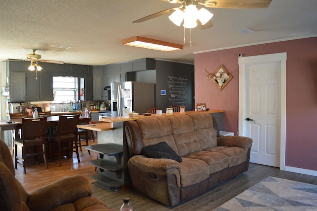 living room with ceiling fan, a textured ceiling, wood finished floors, baseboards, and ornamental molding