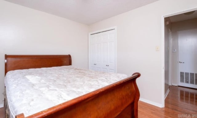 bedroom with baseboards, visible vents, a closet, and wood finished floors