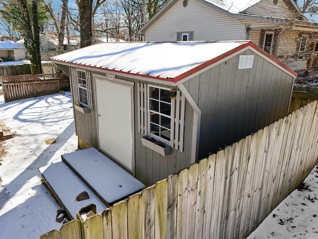 snow covered structure with fence and an outdoor structure