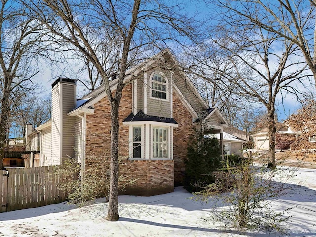 view of snowy exterior featuring a chimney, fence, and brick siding