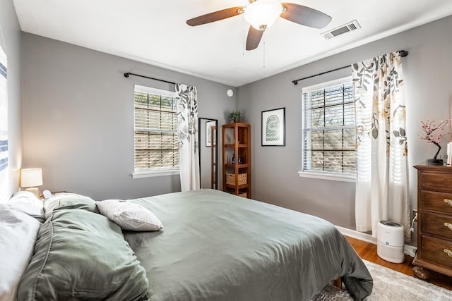 bedroom with baseboards, ceiling fan, visible vents, and wood finished floors