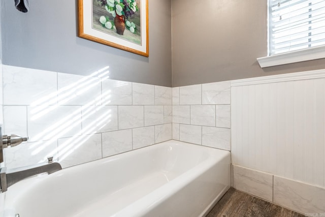 bathroom with wainscoting, wood finished floors, and a bath