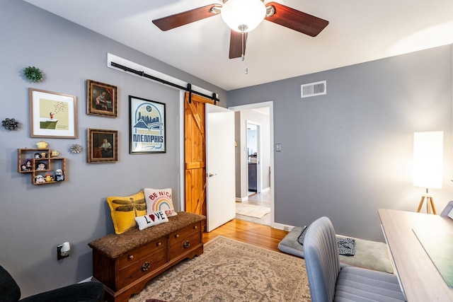 home office featuring light wood finished floors, a barn door, visible vents, baseboards, and a ceiling fan