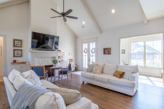 living area with beam ceiling, a tiled fireplace, wood finished floors, and a wealth of natural light