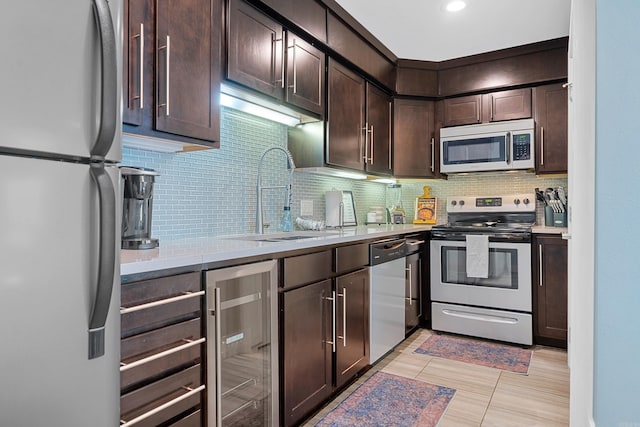 kitchen featuring dark brown cabinetry, beverage cooler, a sink, light countertops, and appliances with stainless steel finishes