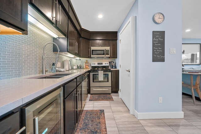 kitchen with wine cooler, dark brown cabinetry, a sink, appliances with stainless steel finishes, and backsplash