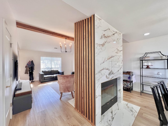 living area featuring a notable chandelier, a premium fireplace, baseboards, light wood finished floors, and beamed ceiling