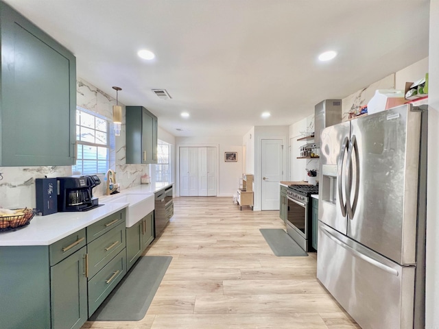 kitchen with light wood finished floors, hanging light fixtures, stainless steel appliances, light countertops, and a sink