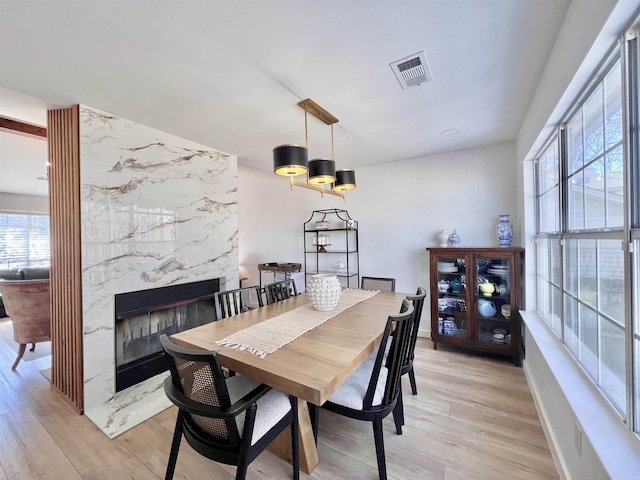 dining area with light wood-style floors, baseboards, visible vents, and a high end fireplace