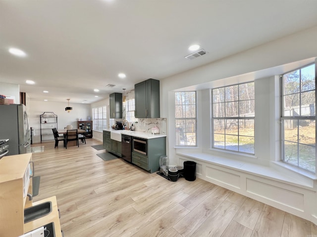 kitchen with visible vents, light wood-style flooring, stainless steel appliances, light countertops, and backsplash