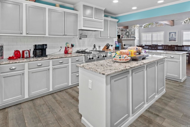 kitchen with a center island, wood finished floors, crown molding, and light stone countertops