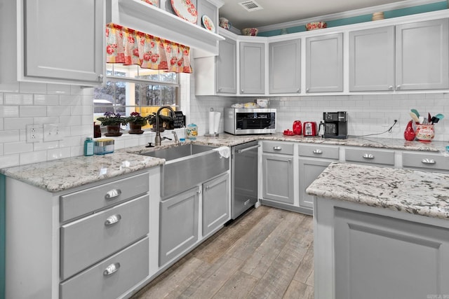 kitchen with light wood finished floors, a sink, stainless steel appliances, gray cabinetry, and backsplash