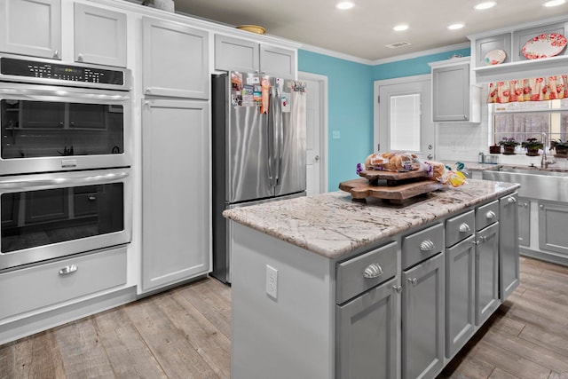 kitchen with light wood-style flooring, appliances with stainless steel finishes, ornamental molding, a sink, and a kitchen island