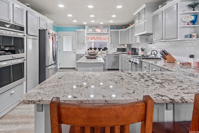 kitchen with a breakfast bar area, open shelves, stainless steel appliances, backsplash, and light stone countertops