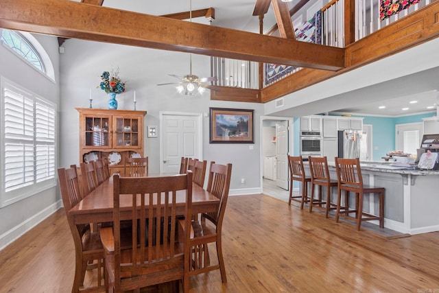 dining room with visible vents, baseboards, a high ceiling, light wood-type flooring, and beam ceiling