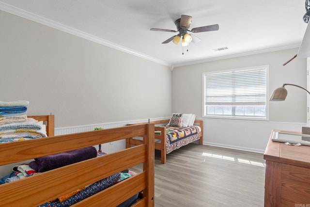 bedroom with light wood finished floors, visible vents, a wainscoted wall, ceiling fan, and ornamental molding