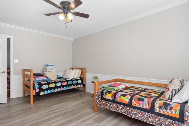 bedroom featuring ornamental molding, a ceiling fan, a wainscoted wall, and wood finished floors