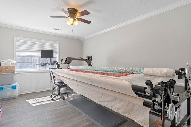 bedroom with ceiling fan, a wainscoted wall, visible vents, light wood-style floors, and crown molding