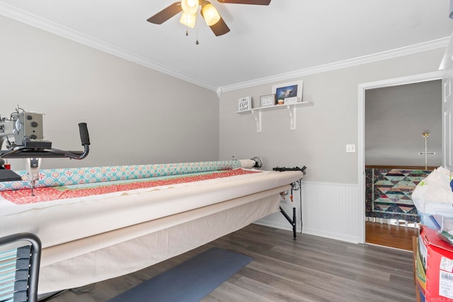 bedroom with crown molding, a wainscoted wall, dark wood finished floors, and ceiling fan