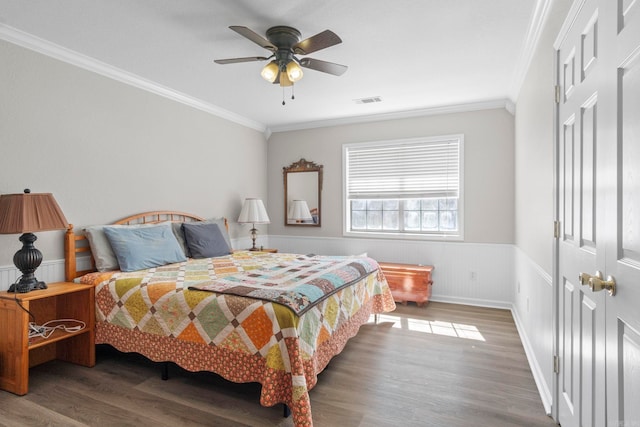 bedroom featuring wainscoting, wood finished floors, visible vents, and crown molding