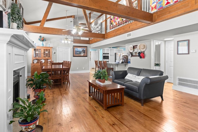 living area with visible vents, light wood-style flooring, a ceiling fan, high vaulted ceiling, and beamed ceiling