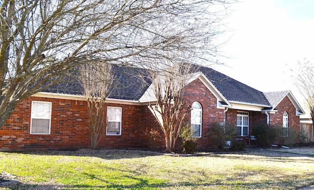 view of front of property with brick siding, a front lawn, and a shingled roof