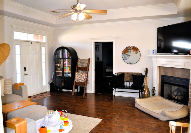 living room with ornamental molding, a tray ceiling, dark wood-style flooring, and a tile fireplace