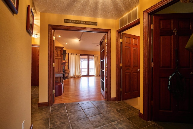 corridor featuring baseboards, visible vents, a textured ceiling, and dark tile patterned flooring