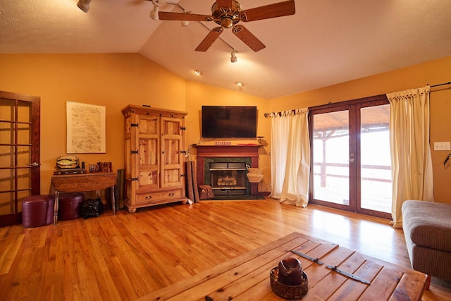 living room with ceiling fan, lofted ceiling, a fireplace, and wood finished floors