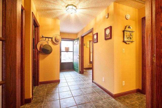 hall featuring dark tile patterned floors, baseboards, and a textured ceiling