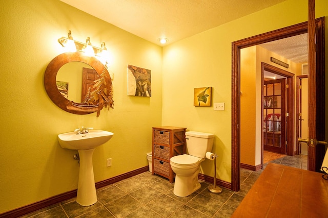 bathroom featuring a textured ceiling, tile patterned floors, toilet, and baseboards