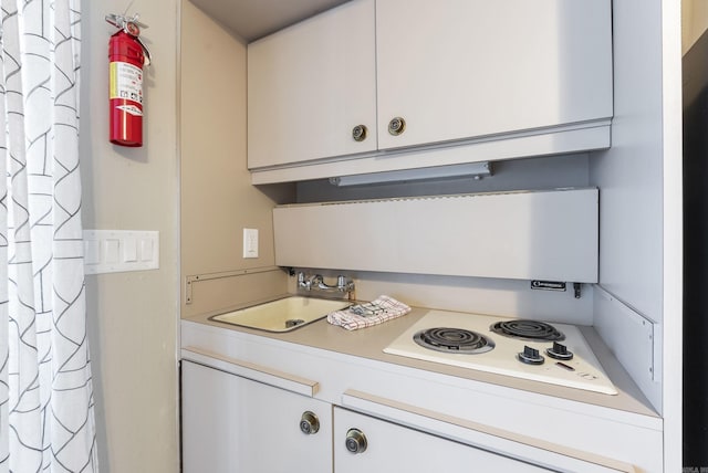 kitchen with white cooktop, a sink, white cabinets, and light countertops