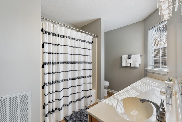 full bath featuring visible vents, toilet, vanity, a textured ceiling, and baseboards