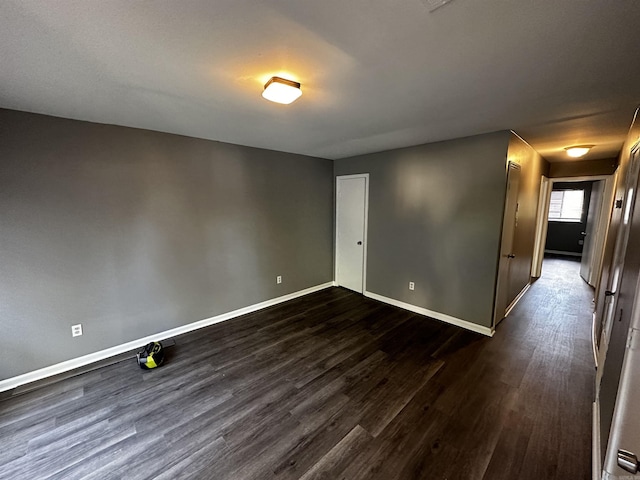 spare room featuring dark wood-type flooring and baseboards