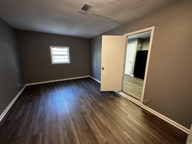 unfurnished bedroom with baseboards, dark wood finished floors, a textured ceiling, and freestanding refrigerator