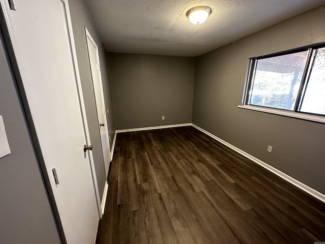 spare room with a textured ceiling, baseboards, and dark wood-style flooring