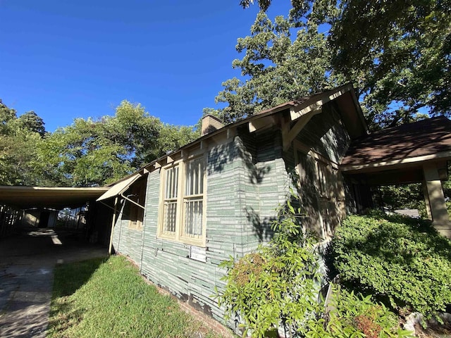 view of property exterior with an attached carport and a chimney