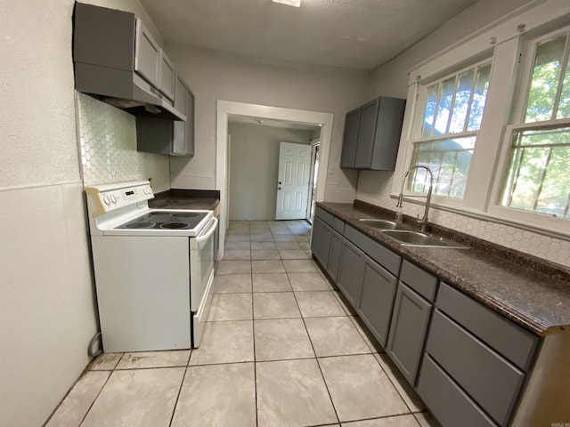 kitchen featuring light tile patterned floors, a sink, electric stove, gray cabinets, and dark countertops