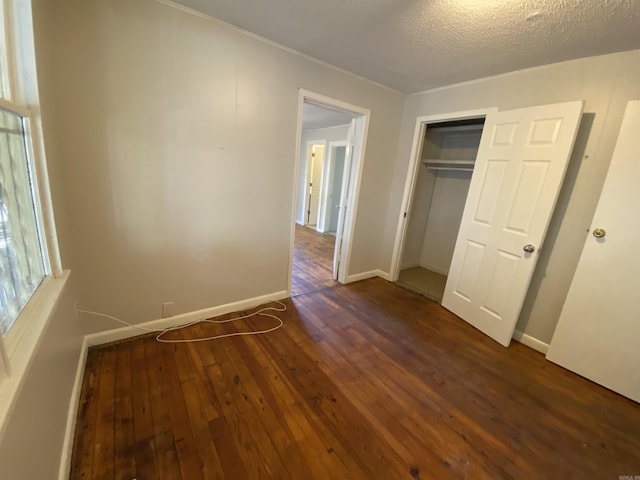 unfurnished bedroom with a textured ceiling, a closet, dark wood finished floors, and baseboards