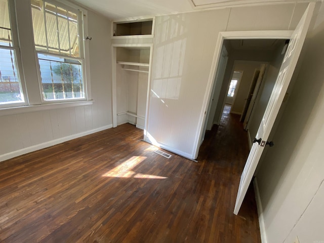 unfurnished bedroom with a closet, dark wood finished floors, visible vents, and baseboards